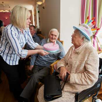 staff offering birthday cake with candles to resident