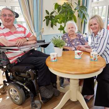 Care home staff sat with smiling residents at table with cups of te